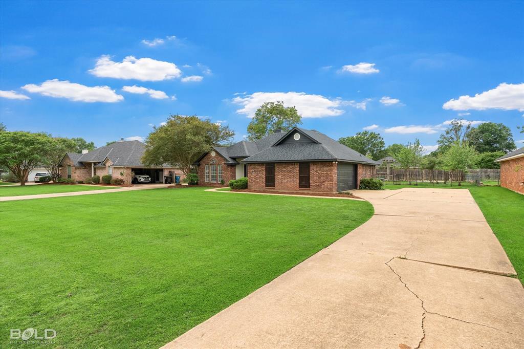 1962 Palmetto Road Benton, LA 71006 - Photo 35 of 40 The property features a brick exterior, a dark shingle roof, a paved driveway, and an expansive lawn