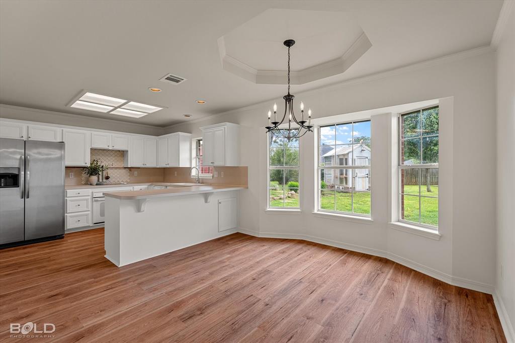 1962 Palmetto Road Benton, LA 71006 - Photo 9 of 40 This open-concept kitchen and dining area features hardwood floors, white cabinetry, a stainless steel refrigerator, and ample natural light from three large windows