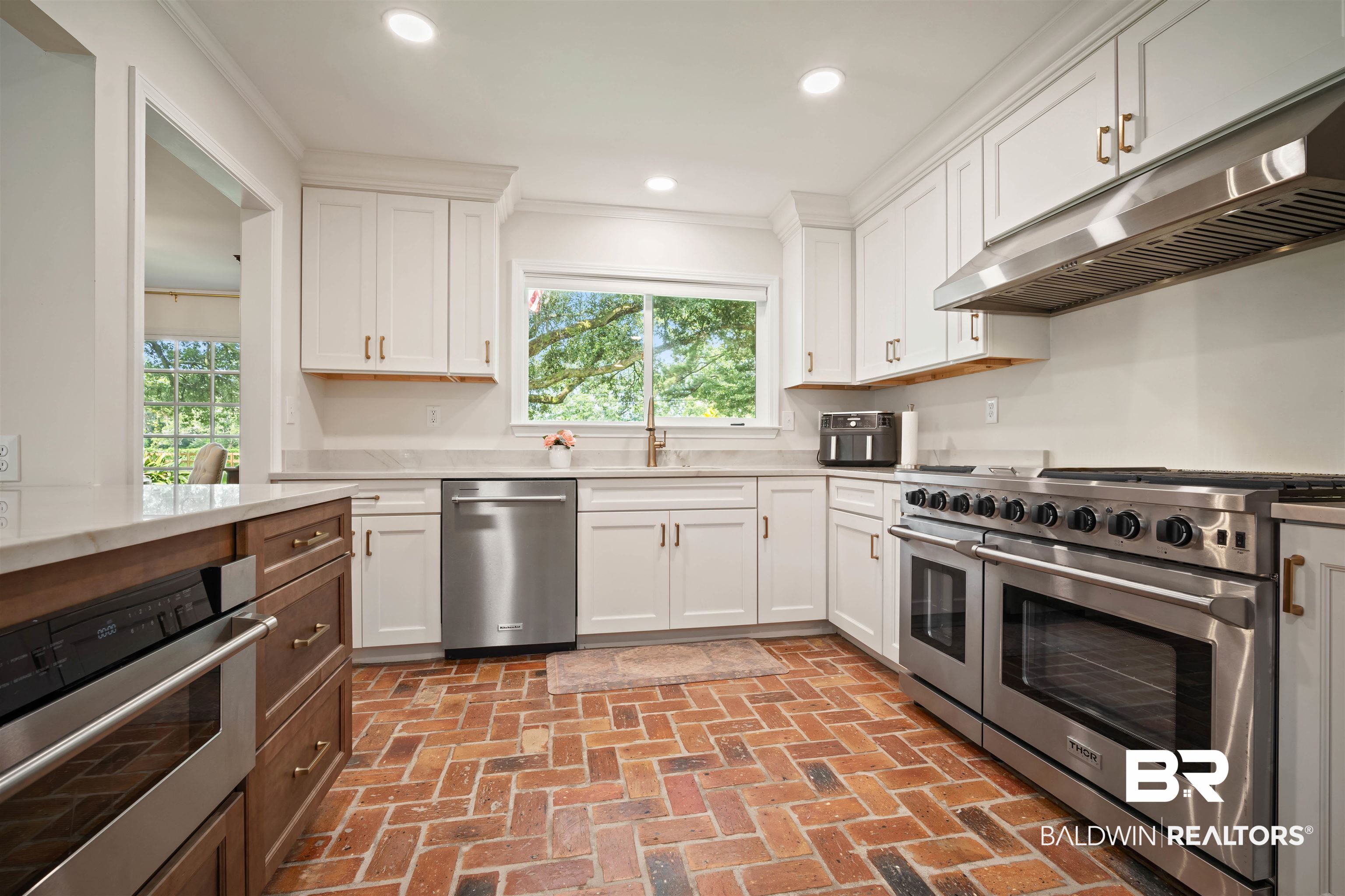 700 Eliza Jordan Road North Mobile, AL 36608 - Photo 17 of 44 Kitchen featuring appliances with stainless steel finishes, crown molding, brick floors, under cabinet range hood, and white cabinetry