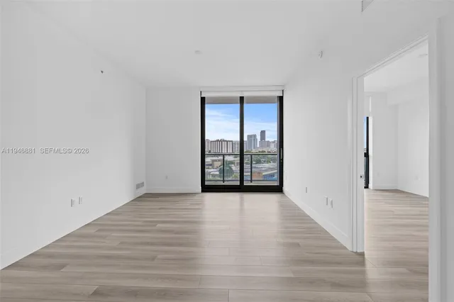a view of an empty room with wooden floor and a window