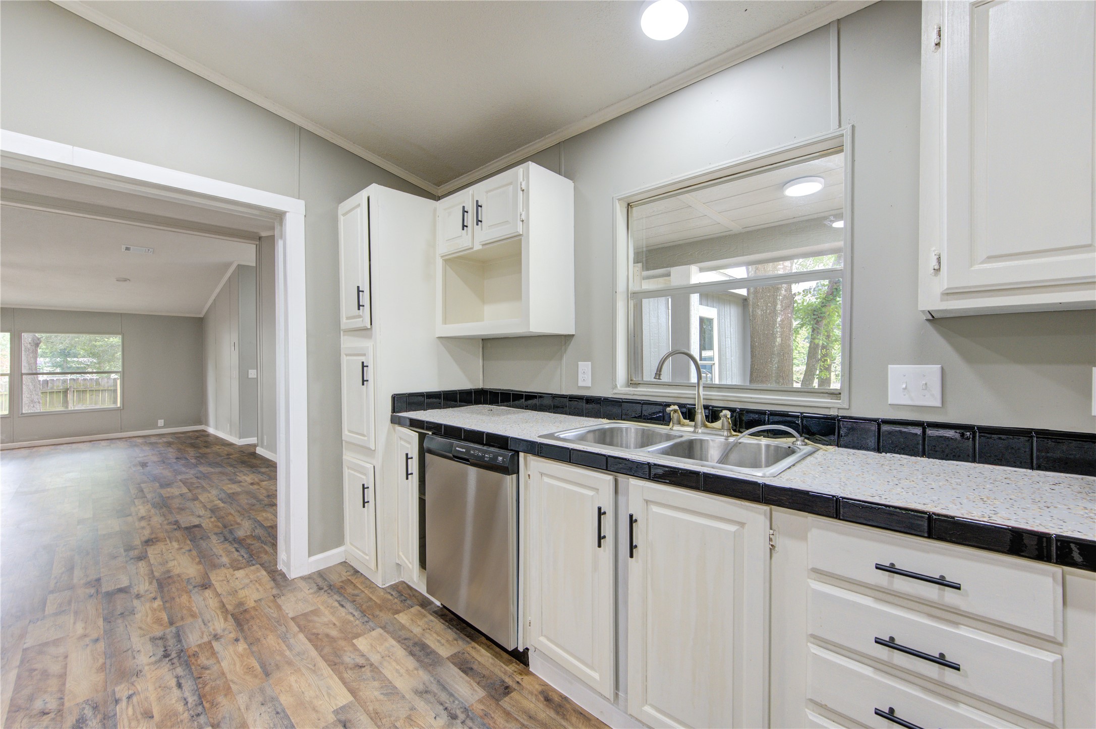 30226 Davis Street Magnolia, TX 77355 - Photo 22 of 50 This kitchen features modern white cabinetry with black hardware, a dual sink, and stainless steel appliances. It opens to a spacious living area with large windows and wood-patterned flooring, creating a bright and inviting space.
