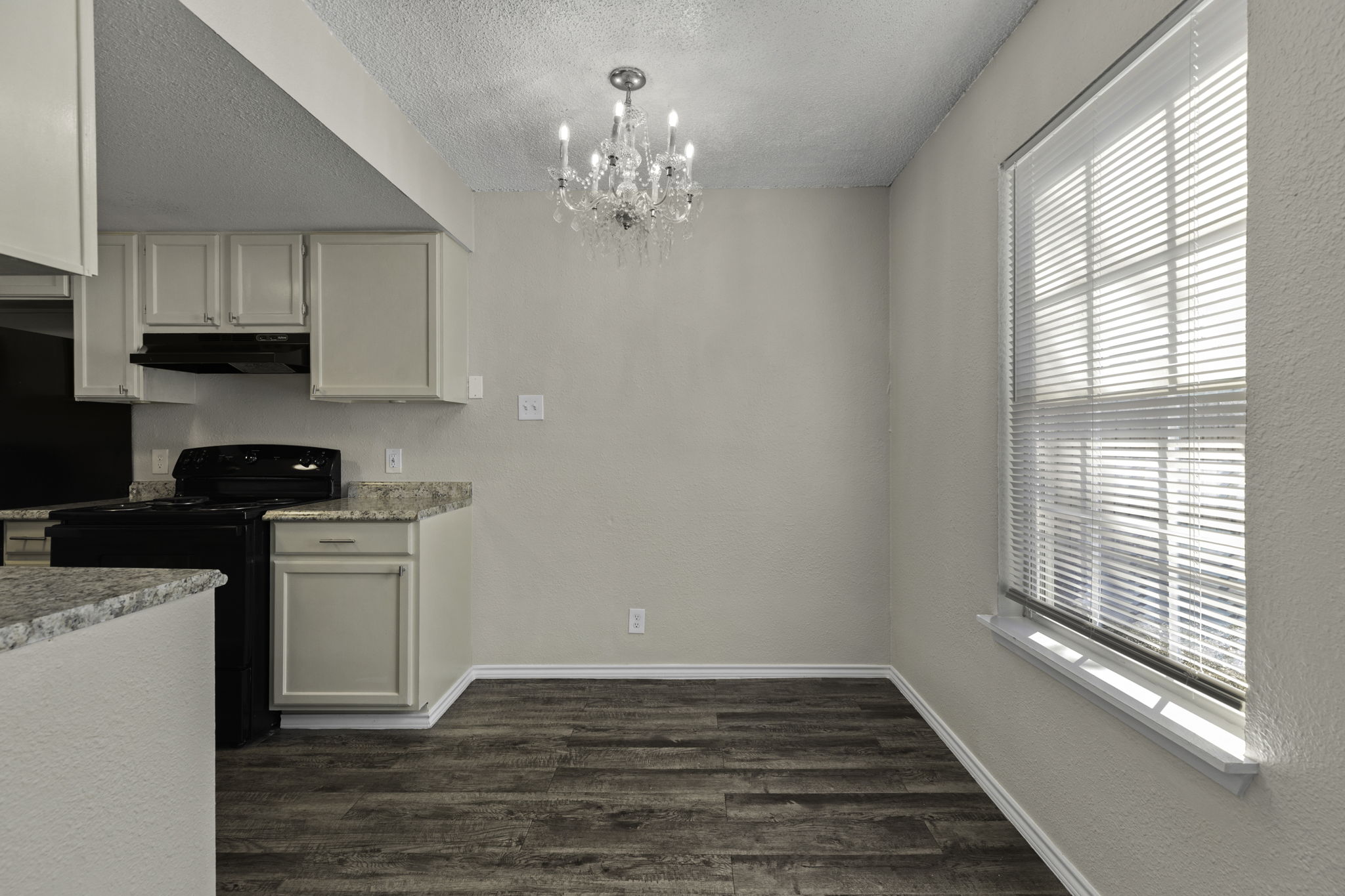 6110 Wheless Cove, Unit E Austin, TX 78723 - Photo 8 of 15 Kitchen with black appliances, a chandelier, a textured ceiling, dark wood-style floors, and light stone countertops