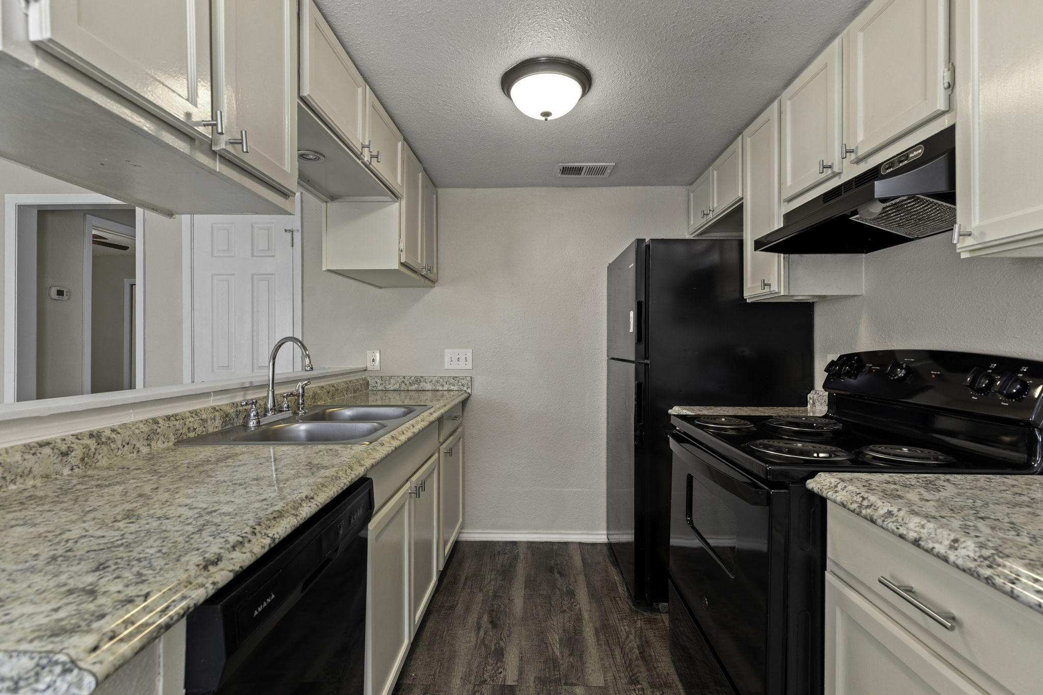 6110 Wheless Cove, Unit E Austin, TX 78723 - Photo 9 of 15 Kitchen featuring black appliances, a textured ceiling, under cabinet range hood, dark wood-style flooring, and light stone counters