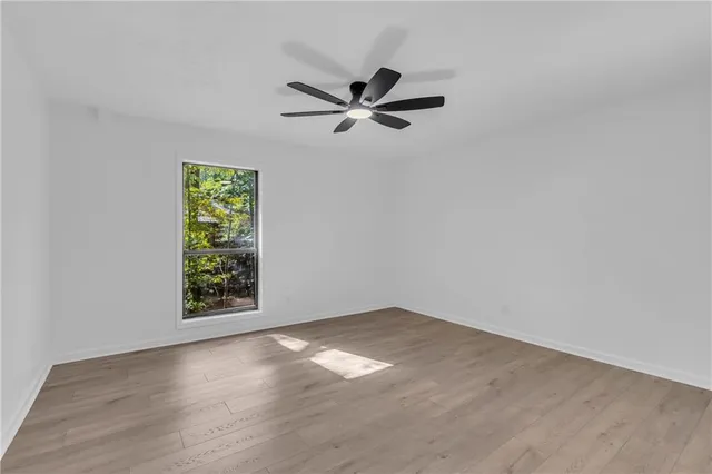 an empty room with wooden floor fan and windows
