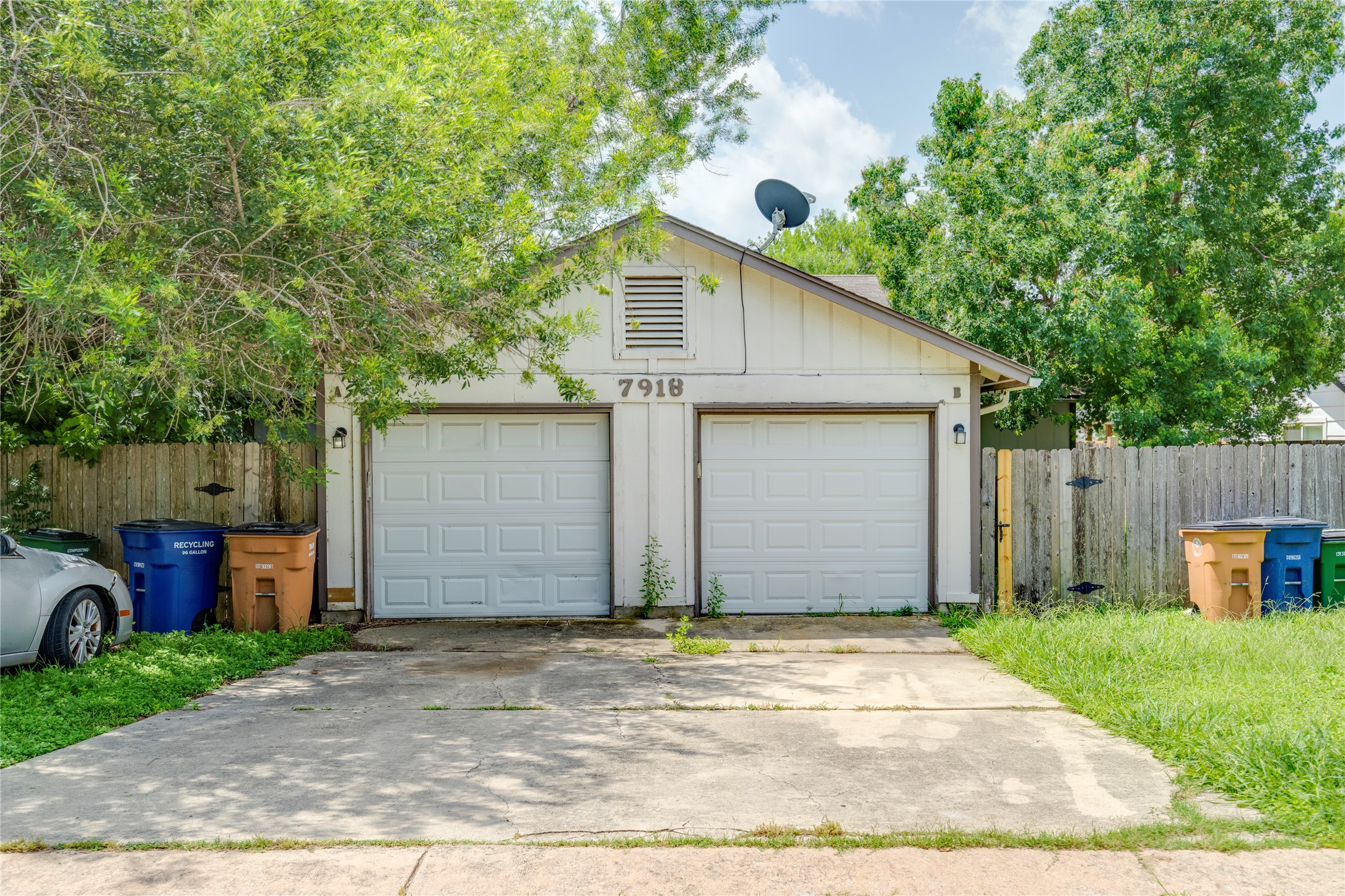 7918 West Gate Boulevard Austin, TX 78745 - Photo 2 of 31 A two-car garage provides ample parking and storage, featuring a concrete driveway and lush green surroundings.