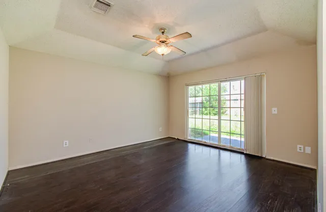 an empty room with wooden floor fan and windows