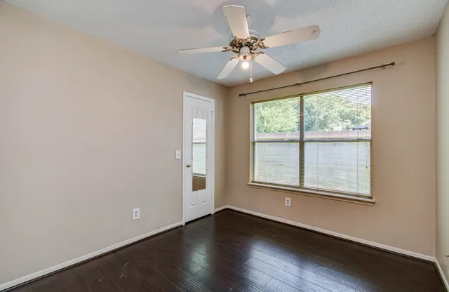 an empty room with wooden floor chandelier fan and windows