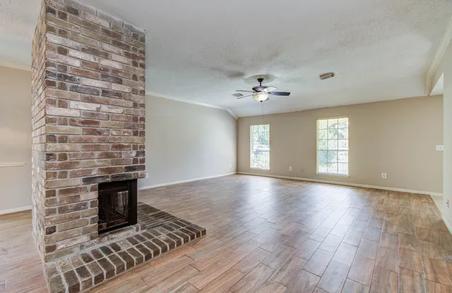 a view of an empty room with wooden floor fireplace and a window