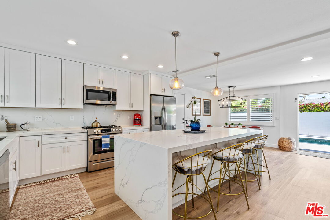 1399 Tamarisk Road Palm Springs, CA 92262 - Photo 8 of 28 a kitchen with stainless steel appliances kitchen island granite countertop a stove a sink a dining table and chairs with wooden floor