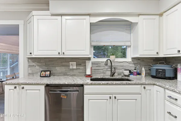 a kitchen with granite countertop stainless steel appliances white cabinets and a window