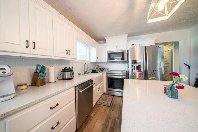 a kitchen with granite countertop a sink dishwasher stove and white cabinets with wooden floor