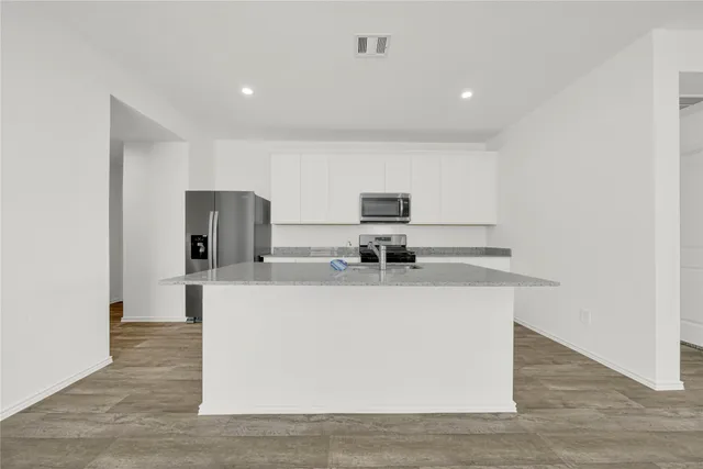 a kitchen with granite countertop kitchen island stainless steel appliances a sink a stove top oven a counter space and cabinets