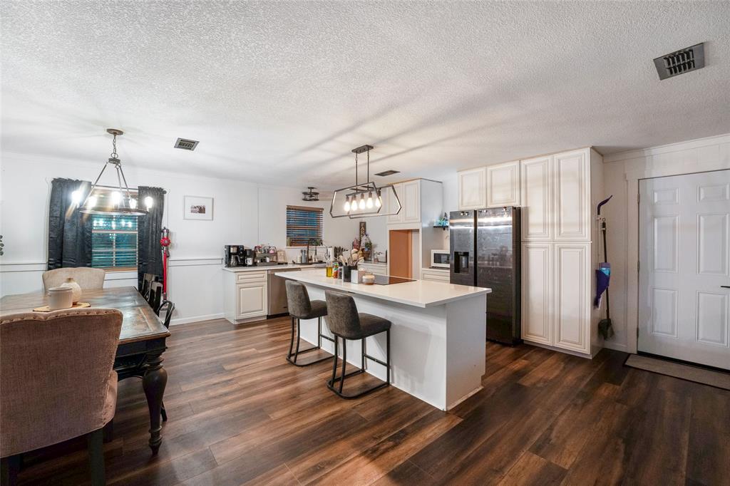 a living room with stainless steel appliances kitchen island granite countertop furniture a refrigerator a sink dishwasher and a dining table with wooden floor