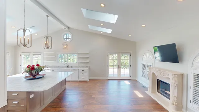 a kitchen with stainless steel appliances granite countertop a sink dishwasher and a flat tv screen next to a large window