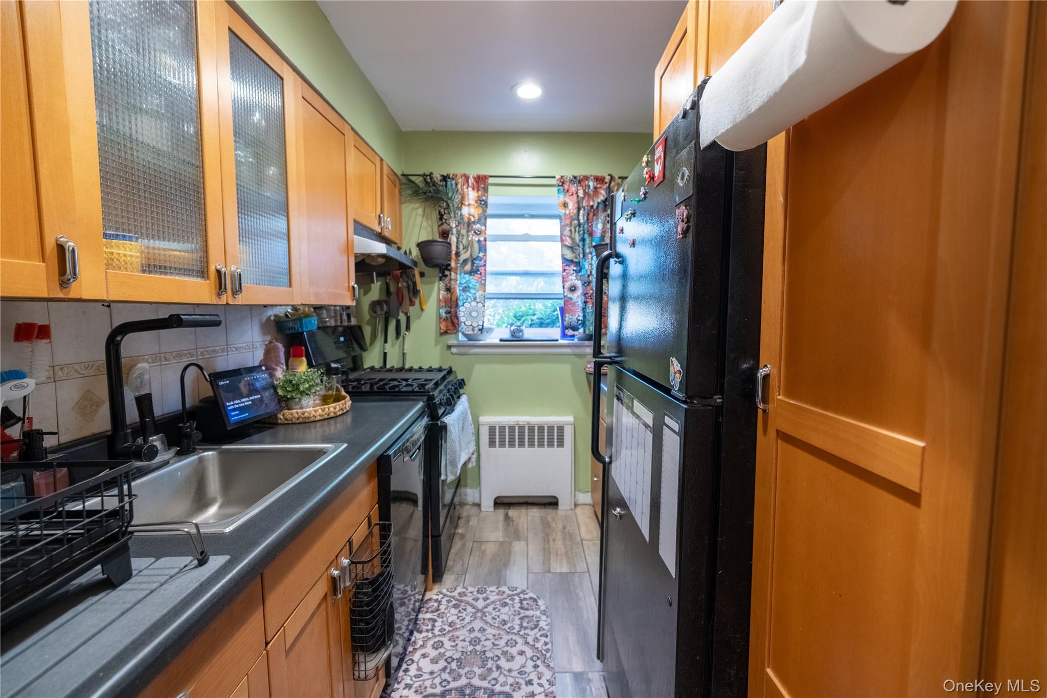 221 Middle Neck Road, Unit M2 Great Neck, NY 11021 - Photo 3 of 15 Kitchen featuring radiator, black appliances, dark countertops, glass insert cabinets, and light wood-style floors