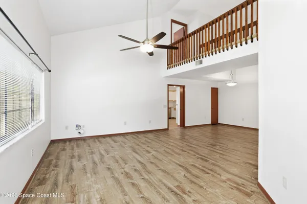 an empty room with wooden floor chandelier fan and windows
