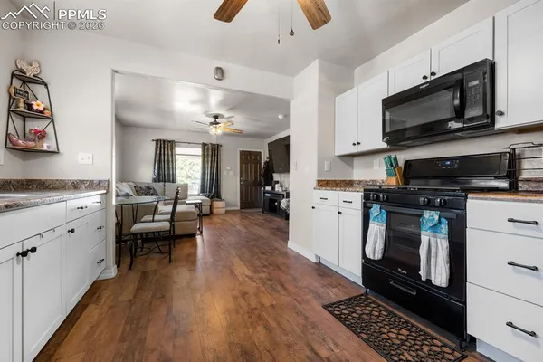 a kitchen with stainless steel appliances kitchen island granite countertop a stove top oven a sink dishwasher and white cabinets with wooden floor