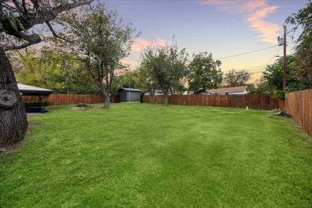 a backyard of a house with large trees and wooden fence