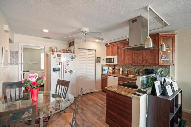 a kitchen with stainless steel appliances granite countertop a stove top oven a refrigerator a dining table and chairs with wooden floor