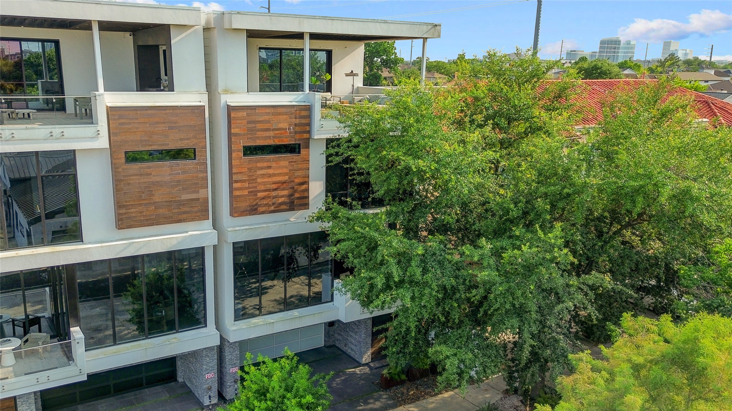 1807 Indiana Street Houston, TX 77006 - Photo 34 of 35 Exterior Elevation: Contemporary four-story architectural masterpiece showcasing a sleek stucco facade, warm wood accent panels, expansive walls of glass, private balconies, and a spectacular top-floor entertaining deck nestled among mature trees.