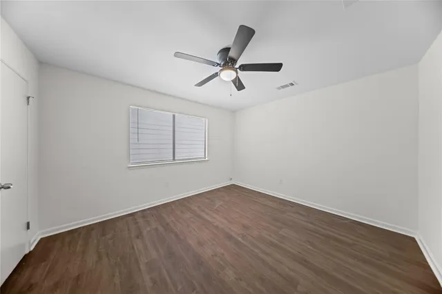 an empty room with wooden floor ceiling fan and windows