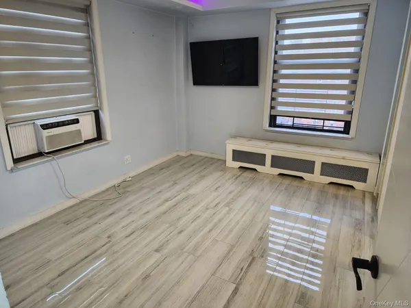 a living room with a flat screen tv on dresser and a wooden floor