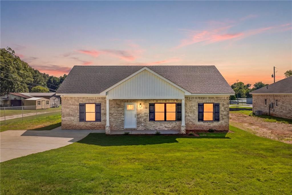 Brick exterior with dark shutters, covered front porch, concrete driveway, and a gabled roof