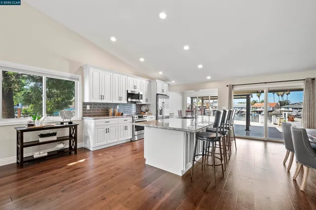 a kitchen with stainless steel appliances kitchen island granite countertop a stove a refrigerator a stove a dining table and chairs with wooden floor
