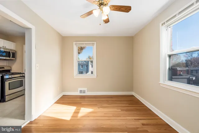 a view of an empty room with wooden floor and a ceiling fan