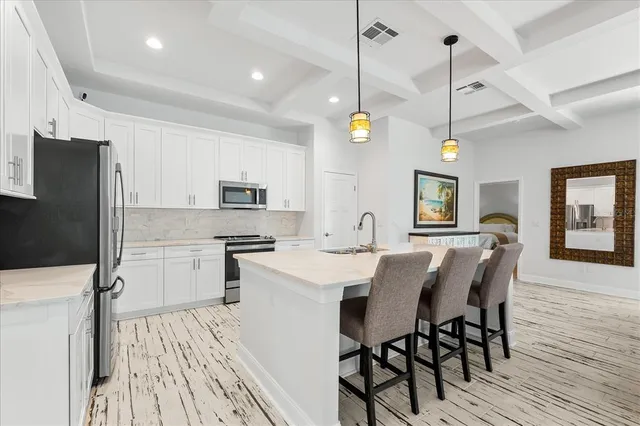 a kitchen with stainless steel appliances kitchen island granite countertop a dining table chairs refrigerator and microwave