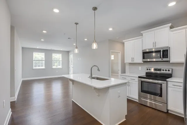 a kitchen with stainless steel appliances granite countertop a sink a stove a microwave oven a refrigerator with white cabinets and wooden floor