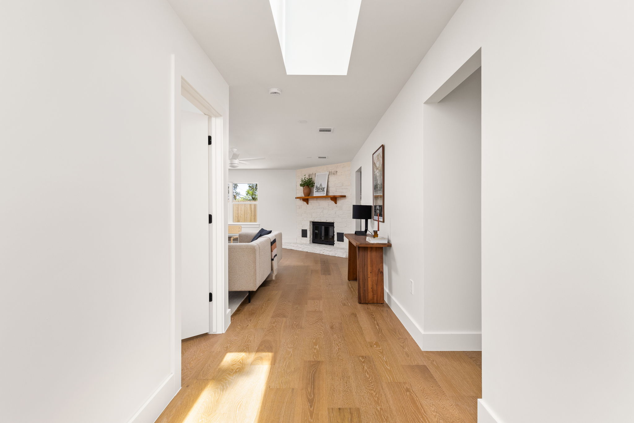 4501 Pack Saddle Pass Austin, TX 78745 - Photo 4 of 37 Hallway with wood-finish flooring, white walls, and a skylight leading into a living area with a white brick fireplace and wooden mantel