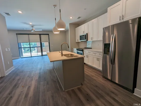 a kitchen with stainless steel appliances granite countertop a refrigerator a sink dishwasher a stove and white countertops with wooden floor