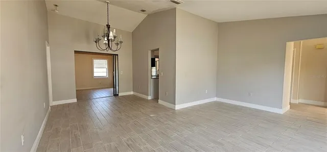 an empty room with wooden floor chandelier and windows