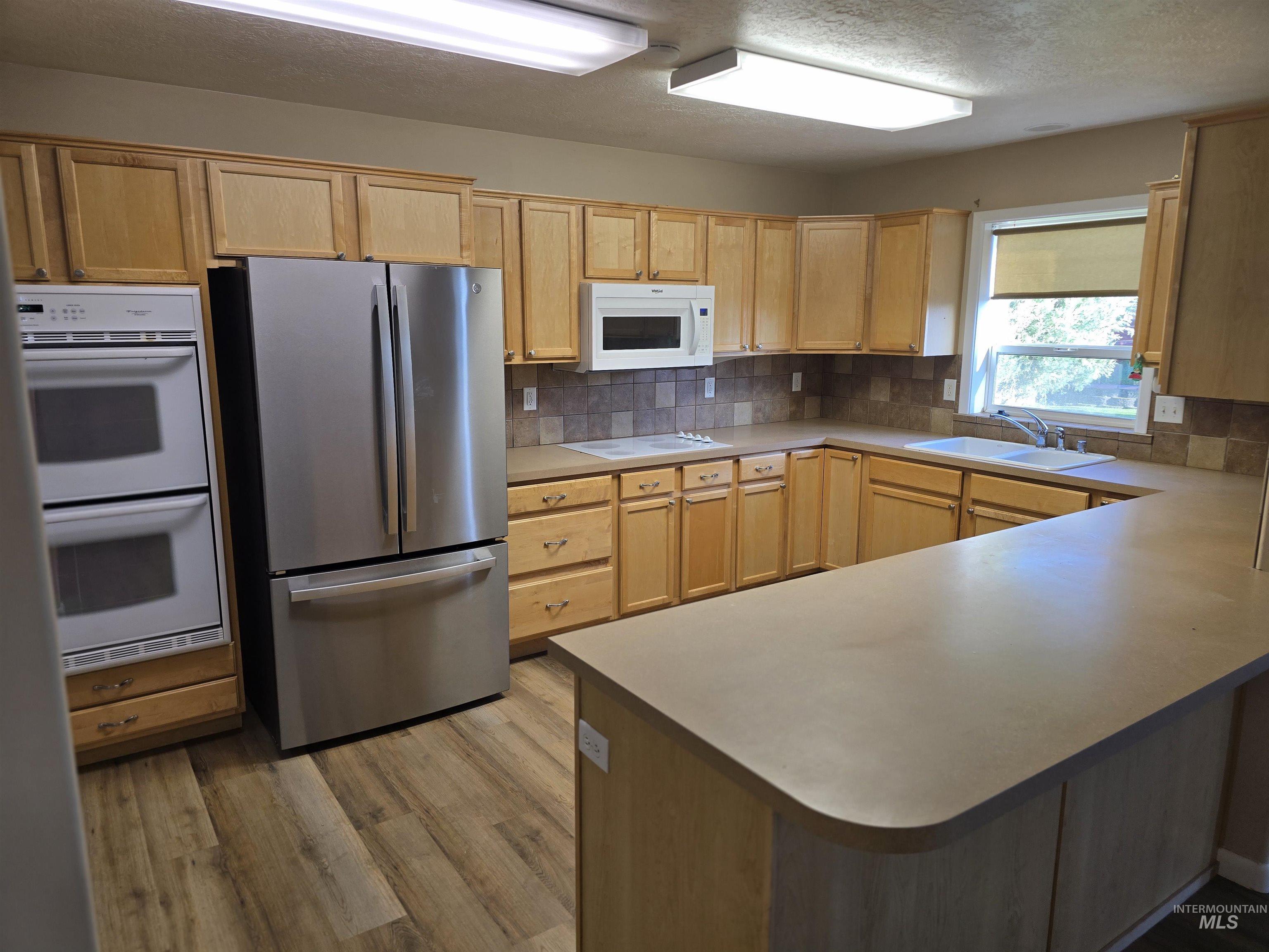 1818 Granada Drive Twin Falls, ID 83301 - Photo 7 of 16 Kitchen with white appliances, light brown cabinetry, decorative backsplash, a peninsula, and a textured ceiling