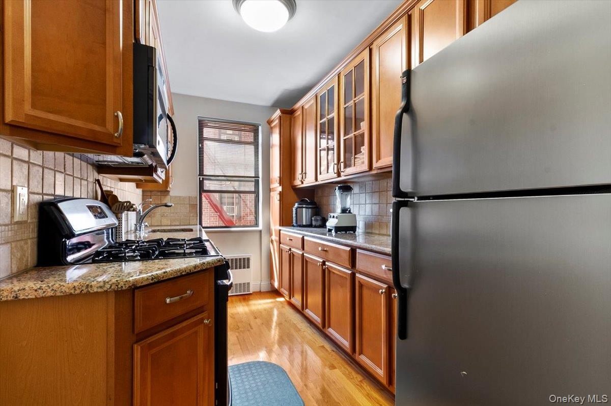 142 Garth Road, Unit 2H Scarsdale, NY 10583 - Photo 3 of 14 Kitchen with stainless steel appliances, brown cabinets, light stone countertops, and glass insert cabinets