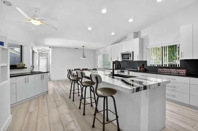 a kitchen with stainless steel appliances kitchen island granite countertop a stove top oven a sink a refrigerator white cabinets and wooden floor