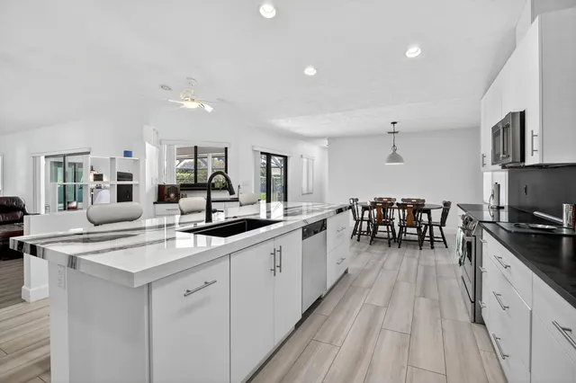 a kitchen with stainless steel appliances kitchen island granite countertop a stove a sink a microwave a dining table and chairs with wooden floor
