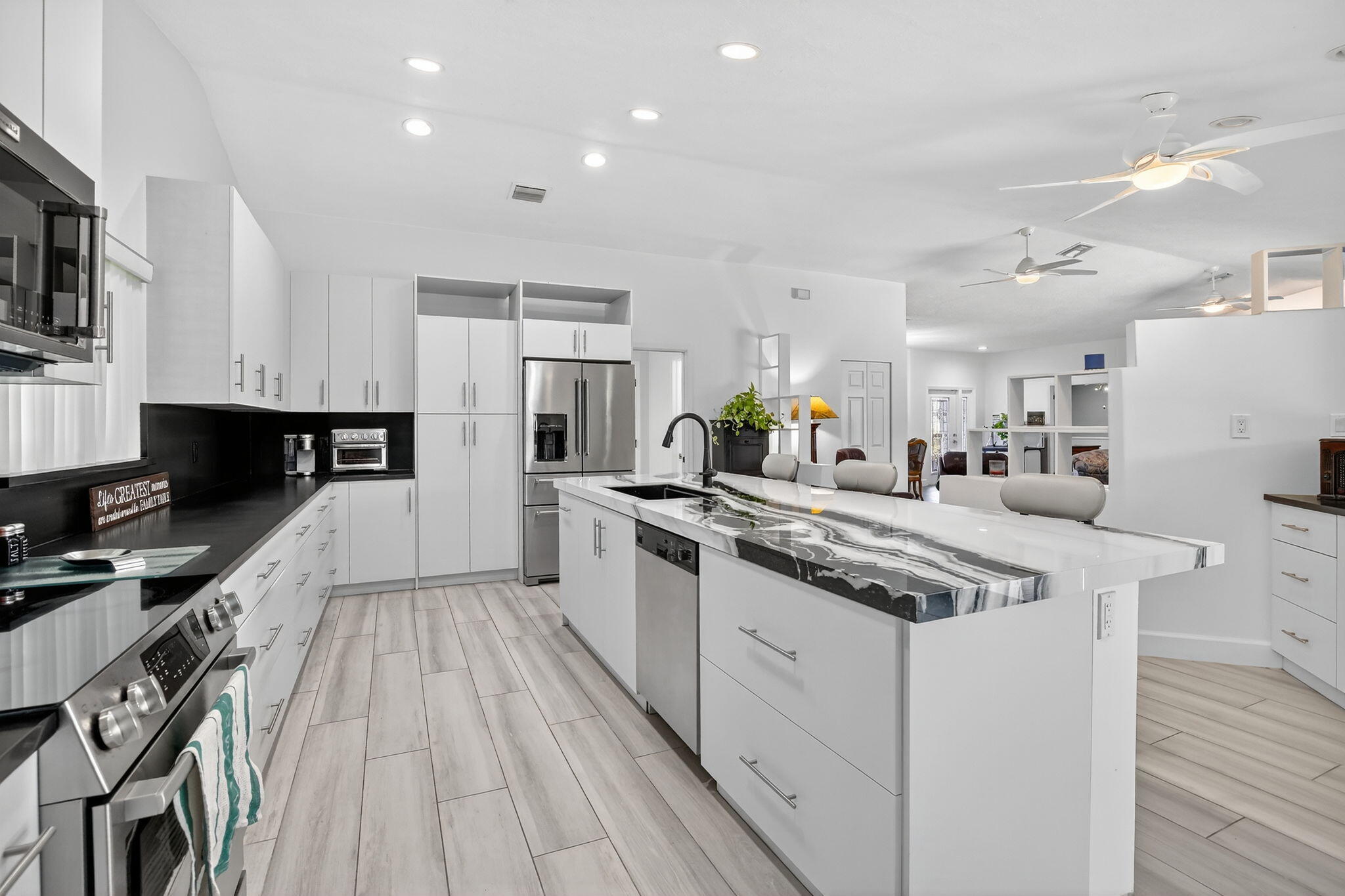 13150 Southwest 16th Court Davie, FL 33325 - Photo 15 of 59 a kitchen with stainless steel appliances kitchen island granite countertop a stove top oven a sink a refrigerator white cabinets and wooden floor