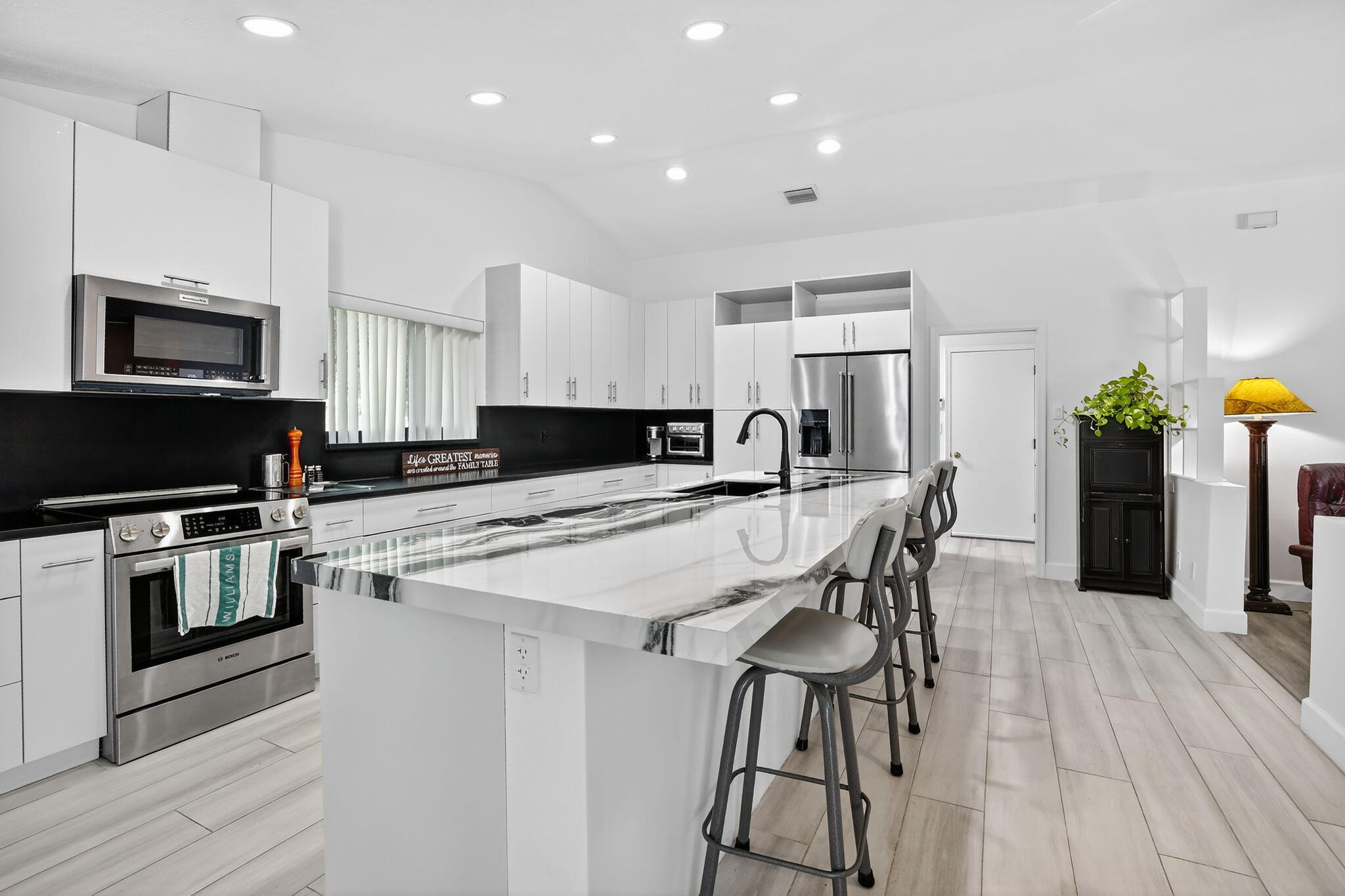 13150 Southwest 16th Court Davie, FL 33325 - Photo 16 of 59 a kitchen with stainless steel appliances kitchen island granite countertop a stove a sink a microwave a dining table and chairs with wooden floor