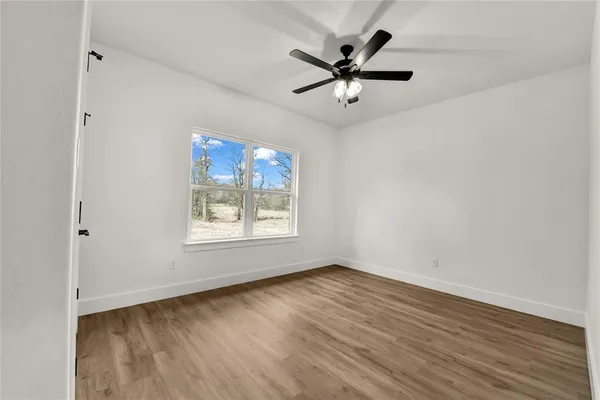 an empty room with wooden floor fan and windows