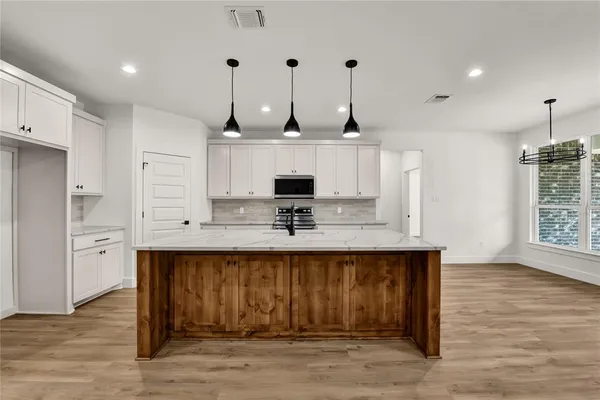 a view of a kitchen with kitchen island a sink wooden floor and stainless steel appliances