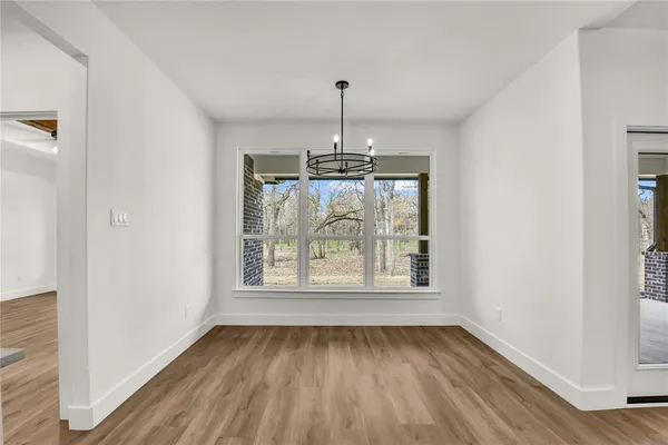 an empty room with wooden floor chandelier and windows