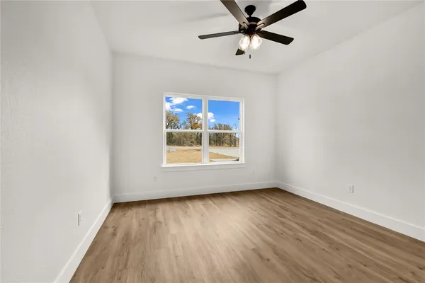 an empty room with wooden floor fan and windows