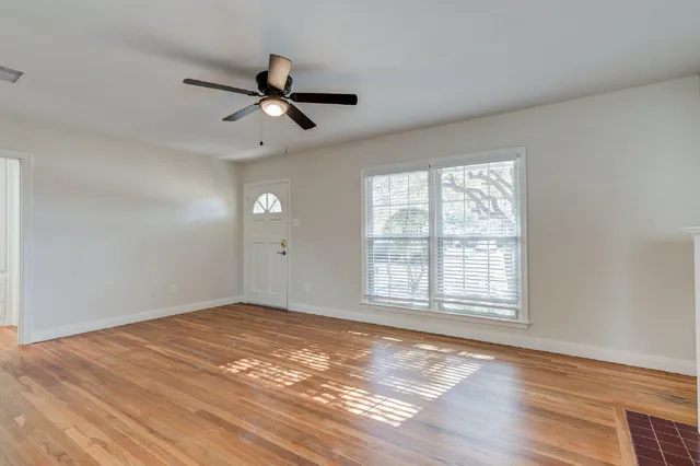 an empty room with wooden floor ceiling fan and windows
