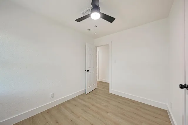 an empty room with wooden floor ceiling fan and windows