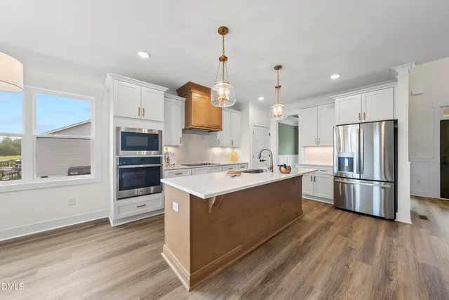 a large kitchen with stainless steel appliances a stove a refrigerator and white cabinets with wooden floors