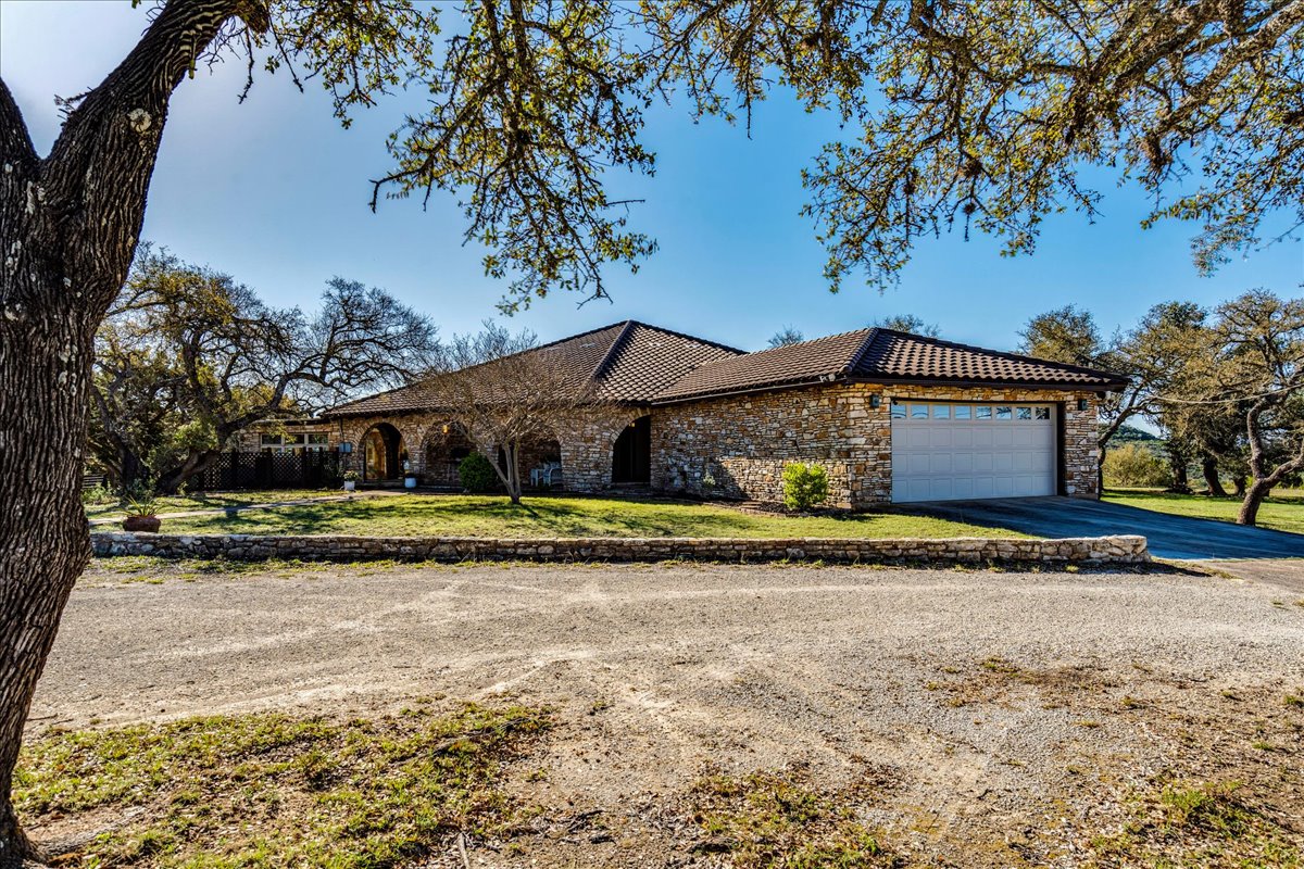 9763 Ranch Road 1623 Blanco, TX 78606 - Photo 3 of 40 View of front facade featuring driveway, a garage, a front yard, stone siding, and a tiled roof