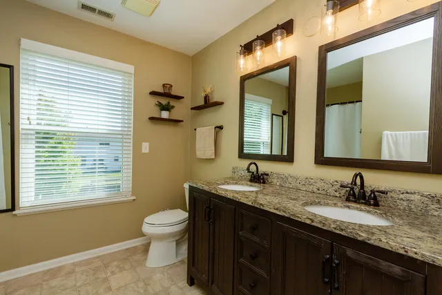 a bathroom with a granite countertop sink toilet a mirror and a window