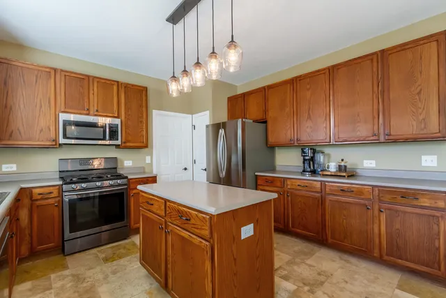 a kitchen with stainless steel appliances granite countertop a stove top oven a sink dishwasher and a refrigerator with wooden cabinets